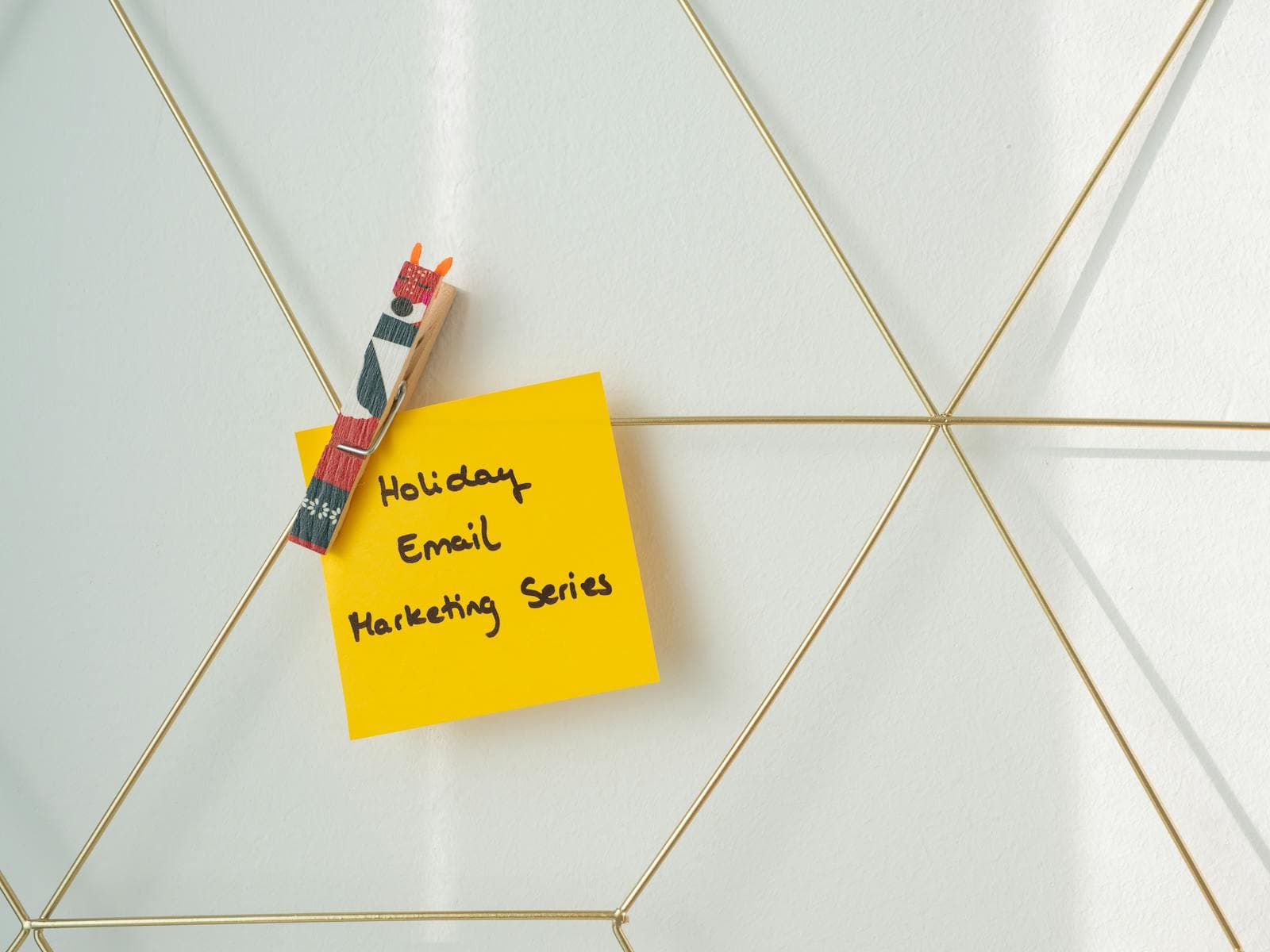 Post-it note with "Holiday Email Marketing Series" attached to a wire grid wall with a decorative clothespin, ideal for holiday email campaign planning.