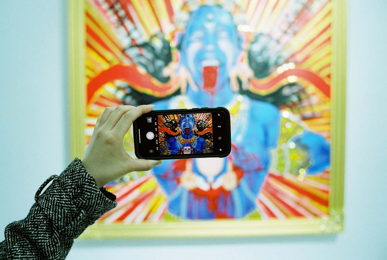 Vibrant artwork of a blue deity with colorful rays on a wall, captured on a smartphone by a visitor.