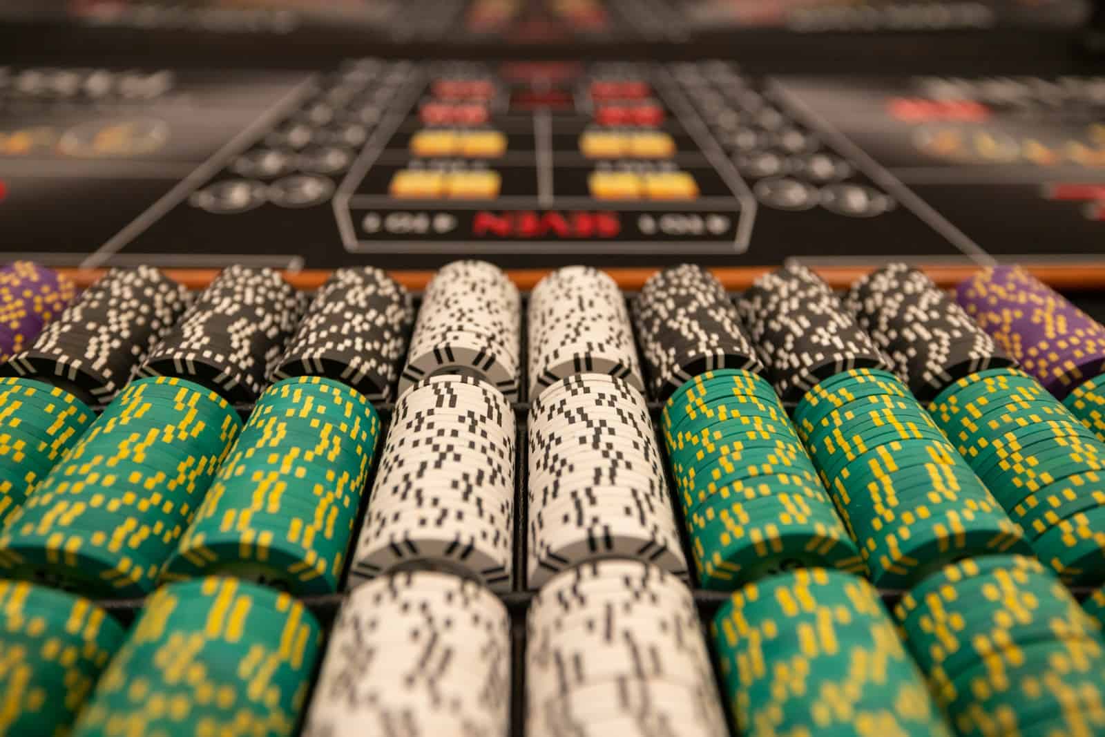 Colorful poker chips stacked on a casino table with blurred gaming layout in the background, representing online and digital gambling entertainment.